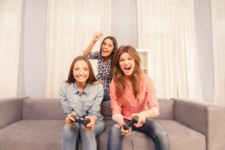 Three happy attractive girls sitting on sofa and playing video gamesの写真素材