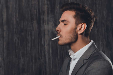 Side view portrait of handsome man in suit smoking a cigaretteの写真素材