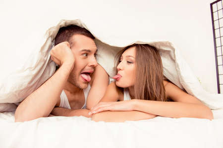 Comic man and woman lying under blanket and showing tongues