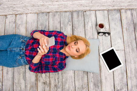 Top view of minded girl lying on floor and typing smsの写真素材