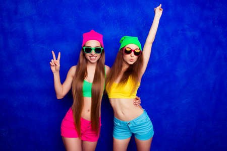Stylish young woman in glasses pouting while her sister gesturing with two fingersの写真素材