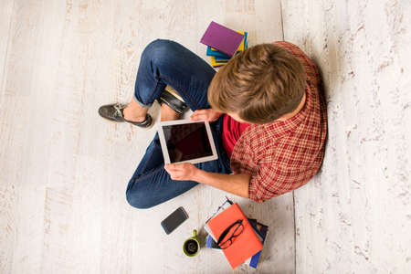Young smart man siting on floor and working with tablet