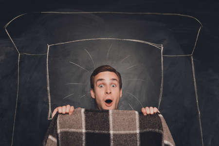 Schocked young man lying with plaid in drawn bedの写真素材