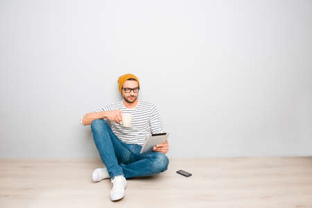 Handsome hipster man in hat and spectacles sitting with tablet and coffeeの写真素材