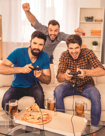 Its a win! excited happy cheerful men play video game with beer and pizzaの写真素材
