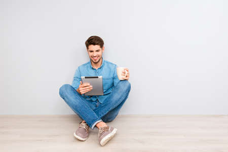 Handsome guy sitting on floor with tablet and crossing legs
