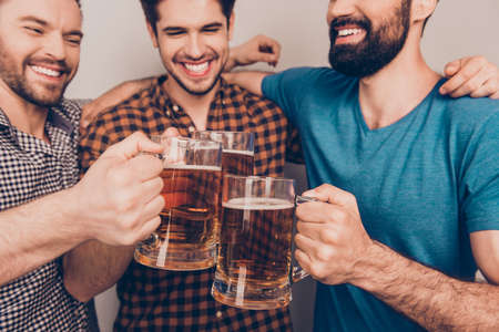 cheers! Close up photo of happy handsome men celebrating victory and clinking glass of beerの写真素材