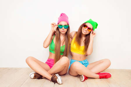 Two trendy girls in glasses siting on floor with crossed legsの写真素材