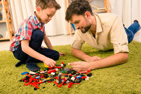 Father and son playing with constructor while lying on carpetの写真素材