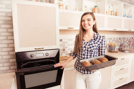 Pretty young woman taking an oven-tray with baked bread from oven