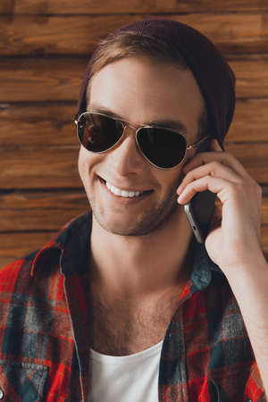 Close up portrait of happy young man in hat and spectakles with smartphoneの写真素材