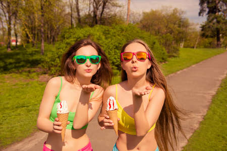 Two beautiful girl walking in park with ice cream and sending air kissの写真素材