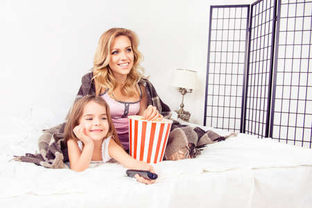 Happy mom and little daughter watching tv with popcornの写真素材