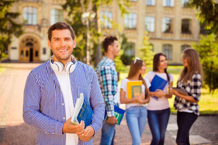 Happy young man holding books while standing university background