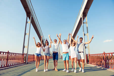 happy group of boyfriends and girlfriends walk bridge with hands up and having fun at summertimeの写真素材
