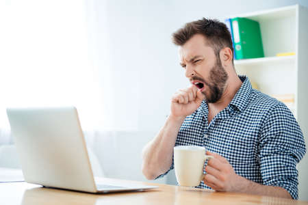 Young businessman yawning and drinking coffee to be energeticの写真素材