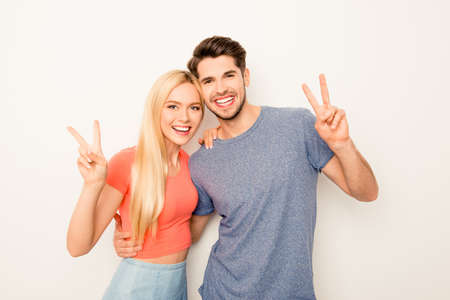 Happy man and woman embracing and gesturing with two fingersの写真素材