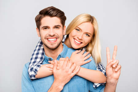 Happy cheerful man carrying his girlfriend on the back and showing two fingersの写真素材
