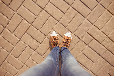 Top view of legs of girl in gumshoes and jeans on pavementの写真素材