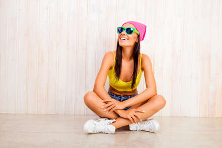 Hipster smiling girl in hat and glasses sitting with crossed legsの写真素材