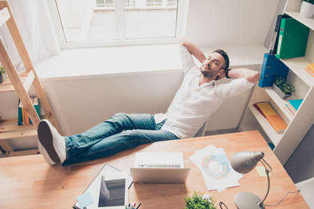 Relaxed happy man sleeping and holding legs on tableの写真素材