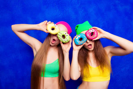 Funny  young girls in hats holding sweet donutes like glassesの写真素材