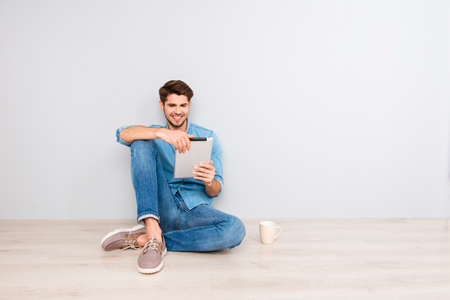 Happy guy sitting on floor with tablet and readingの写真素材