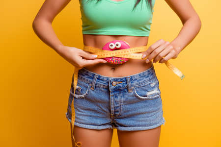 girl  holding pink donut near her belly with centimeter.  she afraid to be fatの写真素材