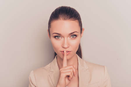 Young pretty businesswoman making silent gesture with finger on lipsの写真素材