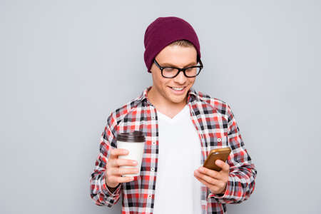 Young hipster in glasses with cup of coffee writing sms on smartphone