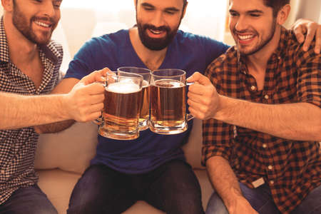 Close up portrait of three happy men clinking with glasses of beerの写真素材