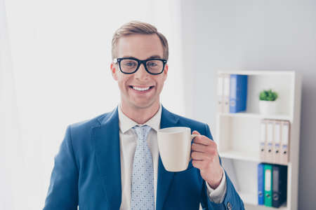 Portrait of happy smiling businessman in glasses holding cup of teaの写真素材
