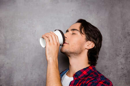 Portrait of young handsome man drinking coffee on gray background