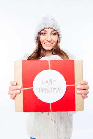 Cheerful woman  in warm hat and scarf holding package and congratulate with xmasの写真素材
