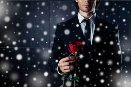 Closeup photo of  man in formalwear  holding red rose on snowy Christmas backgroundの写真素材