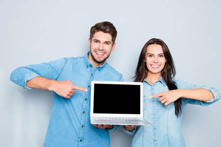 Happy man and woman showing laptop and pointing on black screenの写真素材