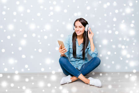 Young happy girl sitting on floor and listening music on winter backgroundの写真素材