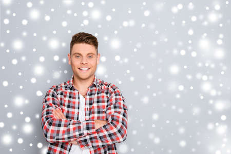 Happy cheerful young guy with crossed hands on the background of snowfall