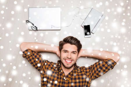 Handsome man lying on floor with different devices on winter background