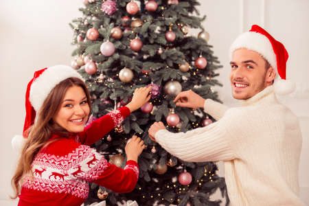 Portrait of happy cheerful man and woman decorating Christmas treeの写真素材