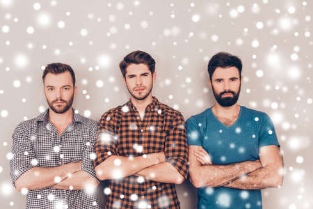Three handsome serious men with crossed hands on snowy winter backgroundの写真素材