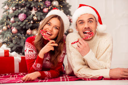 Young happy funny family lying near christmas tree and eating red candy caneの写真素材