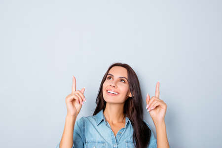 Pretty  young brunette in jeans shirt gesturing up with fingersの写真素材