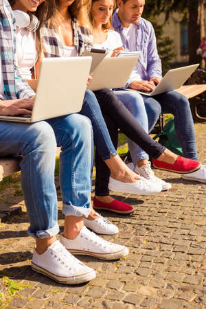 Close up of busy students sitting on bench and studying with laptops