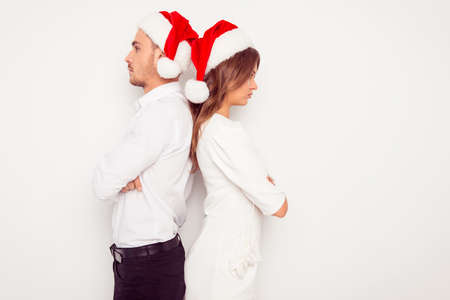 Serious man and woman in santa hats standing back to back on white backgroundの写真素材