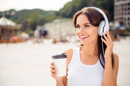 Portrait of happy relaxed woman listening music in headphones and drinking coffeeの写真素材