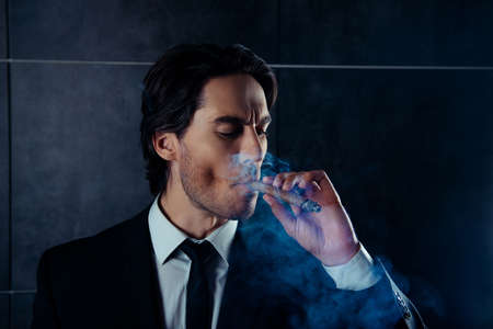 Handsome brutal man smoking a cigar on black backgroundの写真素材