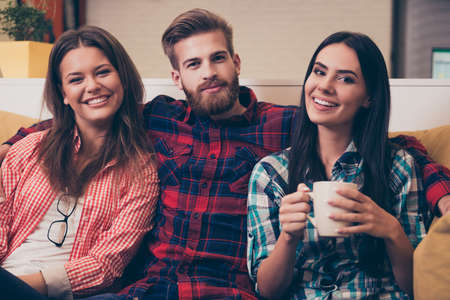 Portrait of young happy man embracing his girlfriends while sitting on sofaの写真素材