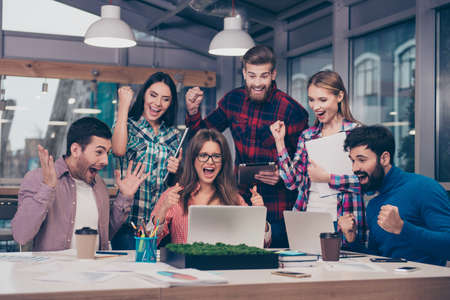 Great news! Happy smiling businesspeople triumphing with raised fists while looking at laptopの写真素材