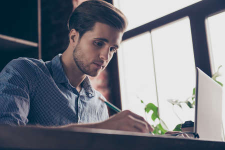 Concentrated handsome young man with laptop making notesの写真素材